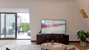 A modern living room with a flat-screen TV on a dark wooden cabinet, a round coffee table, and a sofa with cushions. - 3-bed Penthouse (London)