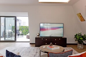 A modern living room with a flat-screen TV on a dark wooden cabinet, a round coffee table, and a sofa with cushions. - 3-bed Penthouse (London)