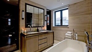 A modern bathroom with a large mirror, dual sinks, a bathtub, and a window providing natural light. - 3-bed Penthouse (London)