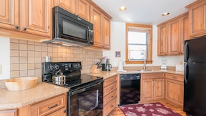 A kitchen with wooden cabinets, a microwave, stove, dishwasher, and a wooden bowl on the counter. - Plunge A by AvantStay | Stunning Views & A Block From Lift #7 (Telluride)