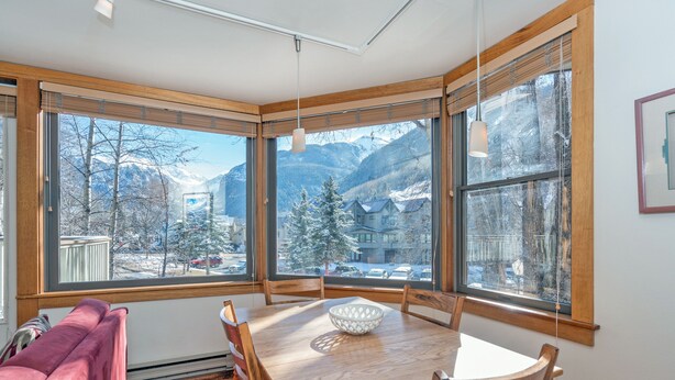 A dining area with a wooden table and chairs, large windows with a view of snow-covered mountains and trees. - Plunge A by AvantStay | Stunning Views & A Block From Lift #7 (Telluride)