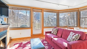 A cozy living room with a red sofa, a wooden bench, and large windows offering a view of snow-covered mountains. - Plunge A by AvantStay | Stunning Views & A Block From Lift #7 (Telluride)
