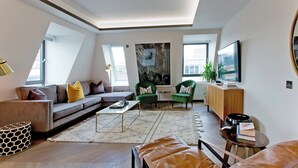 A modern living room with a sectional sofa, green armchairs, a coffee table, and a TV. - 2-bed Deluxe 621 (London)