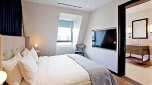 A modern hotel room with a large bed, a TV, a bathroom with a mirror, and a window providing natural light. - 2-bed Deluxe 621 (London)
