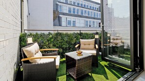 Un patio con mobiliario de mimbre, un ventanal y vistas a un edificio de varios pisos.