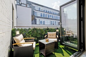 A patio area with wicker furniture, a glass door, and a view of a multi-story building.