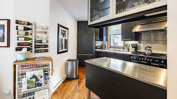 Una cocina moderna con estufa de acero inoxidable, armarios negros y una estantería para vinos en la pared.