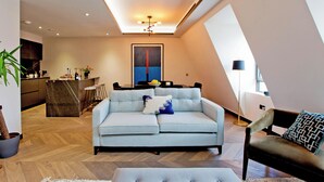Ein modernes Wohnzimmer mit einem hellblauen Sofa, einem Essbereich und einer Küche im Hintergrund.