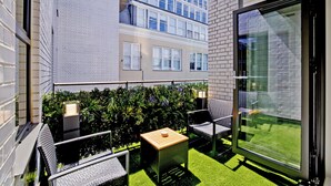 Un balcon aménagé avec du mobilier d’extérieur, une petite table et une porte vitrée donnant sur une zone herbeuse.