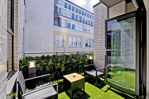 Un balcone con mobili da esterno, un tavolino e una porta vetrata che si apre su una zona verde.