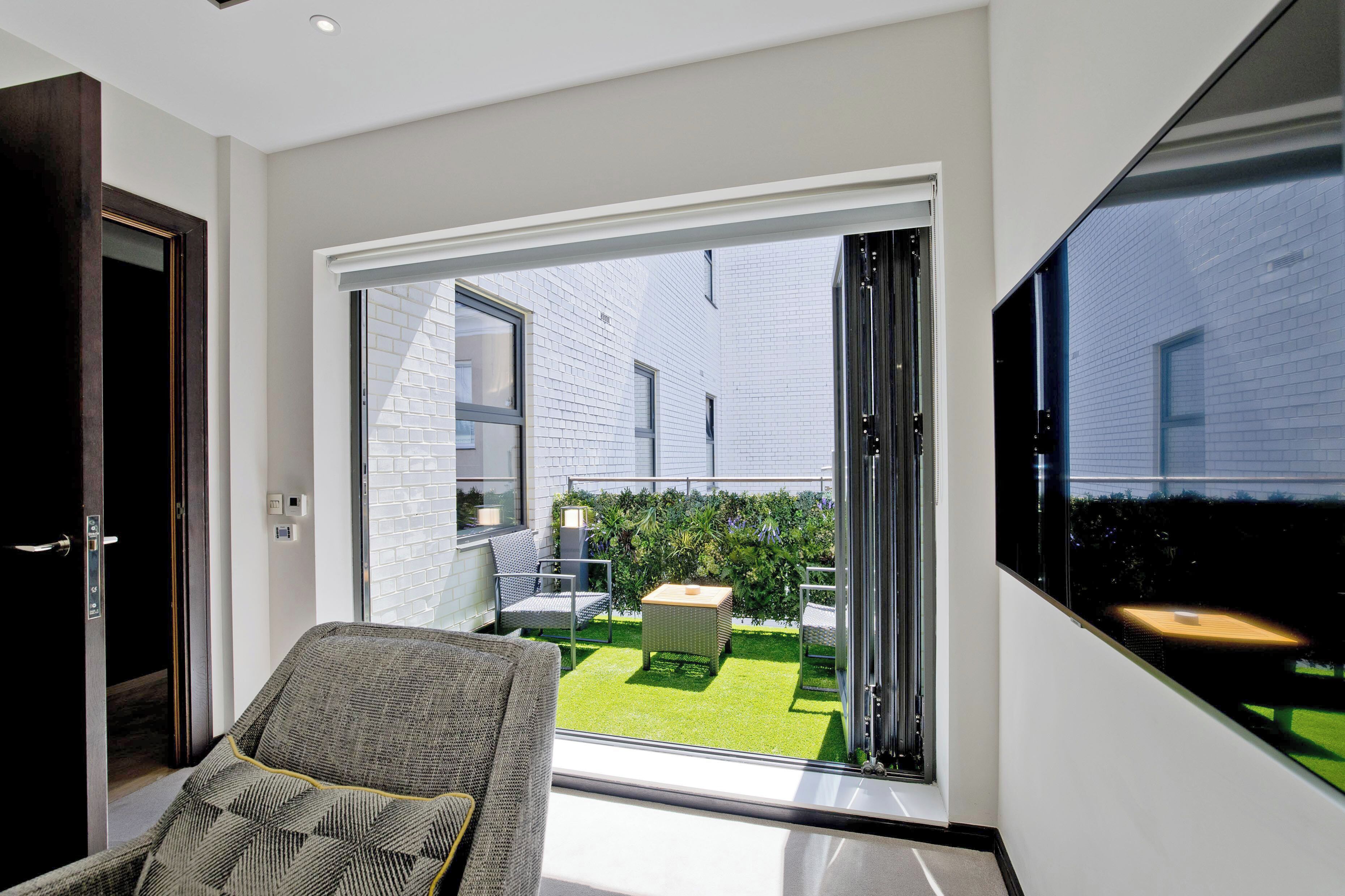 A modern living room with a large sliding glass door leading to a balcony with a view of a brick building and a well-maintained lawn.