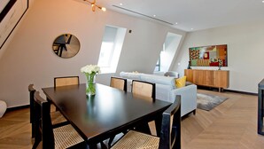 Un salon moderne avec un coin repas, comprenant une table à manger en bois, des chaises en osier, un canapé et un tableau abstrait aux couleurs vives accroché au mur.