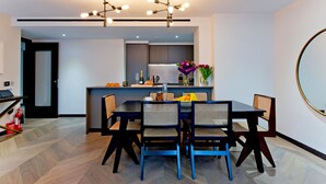 Un comedor moderno con una mesa negra y sillas de mimbre, una cocina al fondo y un espejo redondo en la pared.