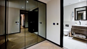 Una habitación de hotel moderna con un separador de vidrio, piso de madera, inodoro blanco y estante empotrado con toallas.