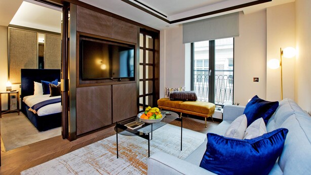 Una habitación de hotel moderna con una cama, un sofá, una mesa de centro con fruta y un televisor.