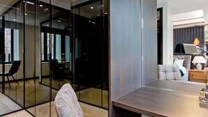 Un interior modern amb una separació de vidre, una zona de dinar amb taula de fusta i un espai de saló amb sofà i làmpada.