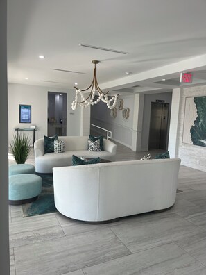 Una hall moderna con un divano bianco curvo, un lampadario e un display digitale.
