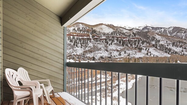 Une terrasse en bois avec deux fauteuils Adirondack donnant sur un paysage montagneux enneigé.