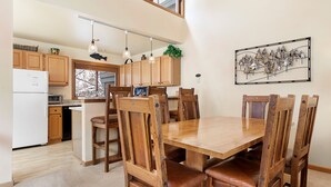 Un coin repas avec une table et des chaises en bois, une cuisine avec des meubles de rangement en bois et un luminaire suspendu.