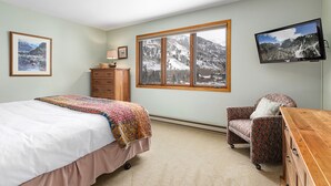 Une chambre à coucher comprenant un lit, une chaise, une commode, un téléviseur et une fenêtre donnant sur la montagne.