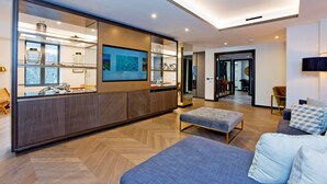 Een moderne woonkamer met een bank, poef en een glazen scheiding met keukenbenodigdheden.