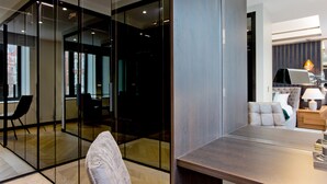 Een modern interieur met een glazen scheidingswand, een eetgedeelte met een houten tafel, en een zithoek met een bank en lamp.