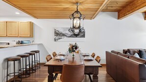 A dining area with a wooden table, bar stools, a sofa, and a chandelier. - River-View Condo • Walk to Lift #8 + Gondola + Downtown | Riverside Condos C102 (Telluride)
