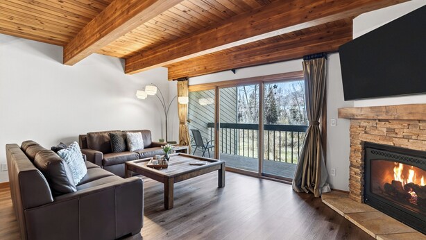 A living room with a fireplace, wooden ceiling, and a large sliding glass door to the outdoors. - River-View Condo • Walk to Lift #8 + Gondola + Downtown | Riverside Condos C102 (Telluride)