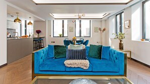 Ein modernes Wohnzimmer mit einem blauen Sofa, einem Glastisch und einem Essbereich im Hintergrund.