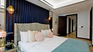 Ein modernes Hotelzimmer mit einem großen Bett, einem Glastisch, einer Wandlampe und einem dunkelblauen Vorhang.