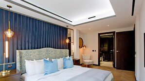 Une chambre d’hôtel moderne, dotée d’un grand lit, d’une table de chevet, d’une chaise et d’une salle de bain visible à travers une porte ouverte.