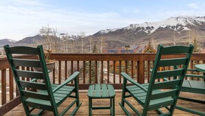 A wooden deck with two green chairs and a small table, overlooking a mountainous landscape with snow-capped peaks. - Russell Home by AvantStay | Expansive Deck, Stunning Views & Hot Tub! (Telluride)
