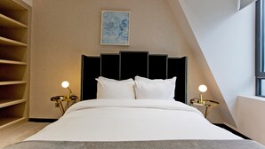 Ein ordentlich bezogenes Bett mit weißen Leinen, einem schwarzen Kopfteil und zwei Nachttischlampen.