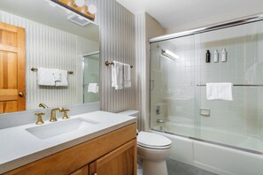 Un baño moderno con un espejo grande, un lavamanos, un inodoro y una zona de ducha con mampara de vidrio.