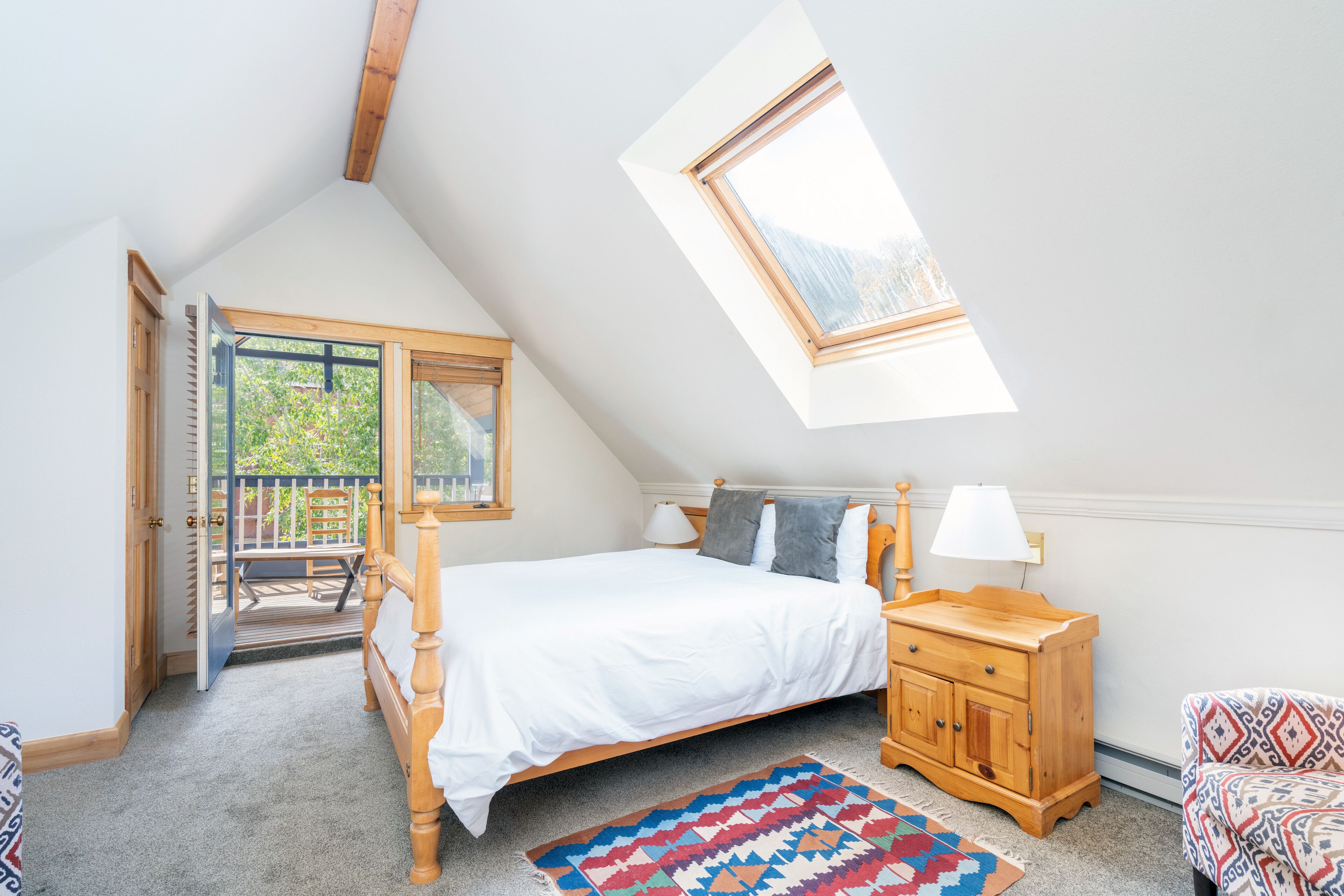 A bedroom with a sloped ceiling, a skylight, a bed, a nightstand, a chair, and a view of the outdoors.