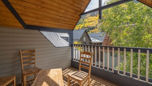 Une terrasse en bois avec une table et des chaises, une rambarde et une vue sur les arbres et les bâtiments.
