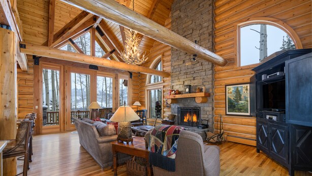 L’intérieur d’une cabane en rondins, avec une cheminée, des meubles en bois et de grandes fenêtres.