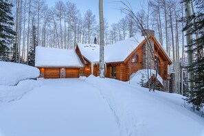 Eine Blockhütte mit schneebedecktem Dach, umgeben von hohen Bäumen und einer verschneiten Landschaft.