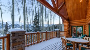 Une terrasse en bois avec un pilier en pierre, une balustrade en bois et une table avec des chaises.