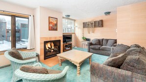 Un salon chaleureux avec des fauteuils en osier, un canapé, une cheminée et une grande fenêtre.
