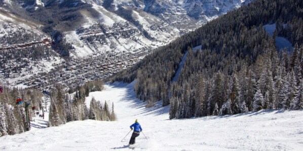 A skier on a snowy slope with a forested mountain backdrop.