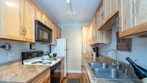 A compact kitchen with wooden cabinets, a microwave, stove, and a sink. - Viking Lodge 103 by AvantStay | Stunning Condo, Near Ski Lift (Telluride)