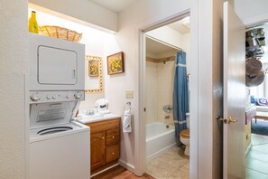 Une petite salle de bain équipée d’un lave-linge, d’un meuble en bois et d’un espace douche agrémenté d’un rideau bleu.