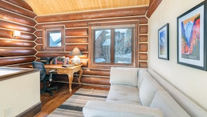 L’intérieur d’une cabane en rondins, avec un bureau en bois, un fauteuil de bureau, un canapé et des tableaux encadrés accrochés aux murs.
