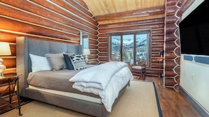Une chambre située dans un chalet en rondins, avec un grand lit, une vue sur des montagnes enneigées et un plafond en bois.