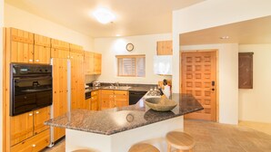 A modern kitchen with wooden cabinets, granite countertops, a large island with stools, and a built-in oven and refrigerator. - Westermere 311 - 2 by AvantStay | Just Steps From Ski Area w/ Great Views! (Telluride)