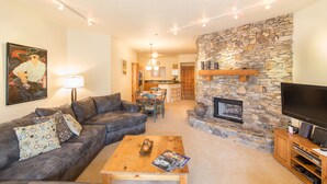 A living room with a stone fireplace, a sofa, a coffee table, and a TV. - Westermere 311 - 2 by AvantStay | Just Steps From Ski Area w/ Great Views! (Telluride)