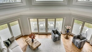 A spacious living room with large windows overlooking a body of water, a wooden coffee table, and two grey armchairs. - Tilghman Waterfront | Indoor Pool | Private Dock | Pool House (Tilghman)