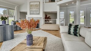 A spacious living room with a high ceiling, a fireplace, and a view of the outdoors. - Tilghman Waterfront | Indoor Pool | Private Dock | Pool House (Tilghman)