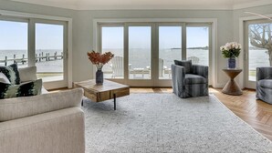 A spacious living room with large windows overlooking a beach, a coffee table, and two armchairs. - Tilghman Waterfront | Indoor Pool | Private Dock | Pool House (Tilghman)